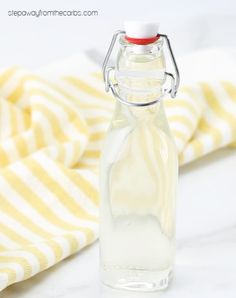 a glass bottle filled with white liquid sitting on top of a table next to a striped cloth