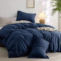 a bed with blue comforters and pillows in a room next to a potted plant