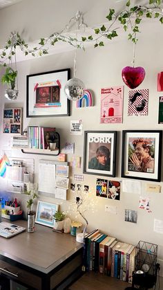 a desk with many pictures and plants hanging from it's wall above the desk