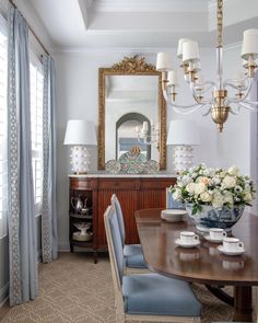 a dining room table with blue chairs and white flowers on the centerpiece in front of a large mirror