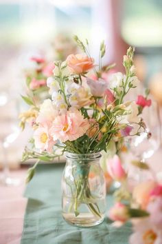 a vase filled with pink and white flowers on top of a green table cloth covered table