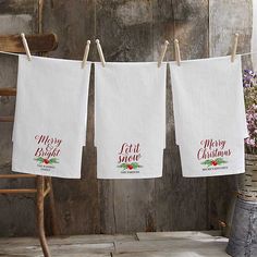 three white towels hanging from a clothes line with merry christmas lettering on them, next to an old wooden chair