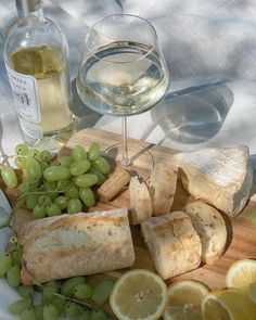 a wooden cutting board topped with sliced up lemons and grapes next to a bottle of wine