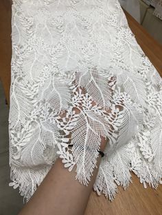 a woman's hand on top of a table covered in white lacy fabric and lace