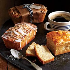 some food is on a black plate with a cup of coffee and two spoons