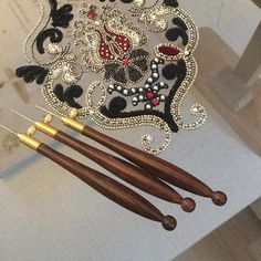 three wooden knitting needles sitting next to each other on a white tablecloth with black and red beading