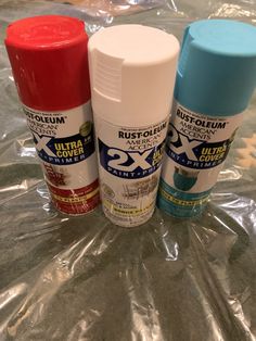 three different types of spray paint sitting on top of a plastic wrap covered tablecloth