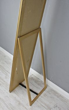 a gold framed mirror sitting on top of a wooden floor next to a gray wall