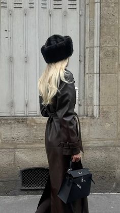 a woman walking down the street wearing a black hat and coat with fur on it