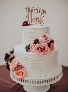 a white wedding cake with pink flowers and mr and mrs topper on the side