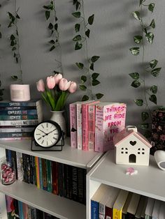 a shelf with books, flowers and a clock on it next to a wall mounted plant