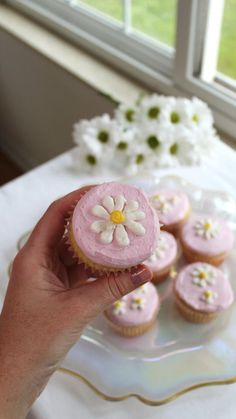 a hand holding a pink cupcake with white flowers on it