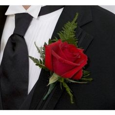 a man wearing a black suit and tie with a red rose in his lapel