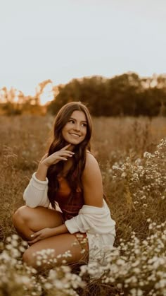 a woman kneeling down in a field with flowers