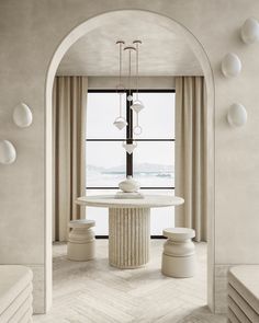 a dining room with an archway leading into the living room, and a round table surrounded by white stools