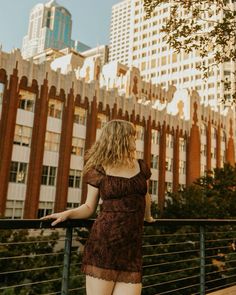 a woman is standing on a railing in front of some buildings and looking at the sky