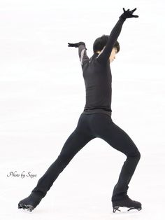 a male figure skating in a black outfit and his arms are stretched out to the side