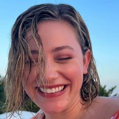 a close up of a person smiling with water on her face and trees in the background