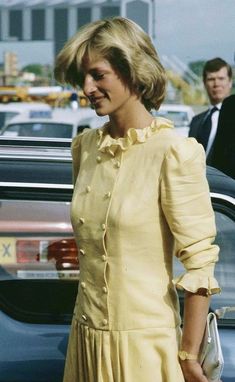 a woman in a yellow dress is standing next to a car and two men are walking behind her