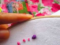 someone is stitching something with pink and purple beads on the side of a white piece of fabric