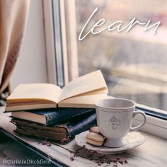 an open book and cup sit on a window sill next to a pair of books