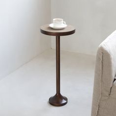 a small table with a cup on it next to a couch in a white room