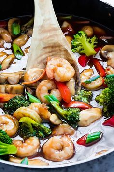 shrimp and broccoli stir fry in a pot with a wooden spoon sticking out of it