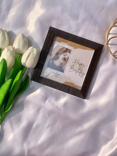 some white tulips are laying next to a photo frame