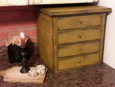 a small wooden dresser next to a brick wall with a lit candle on the top