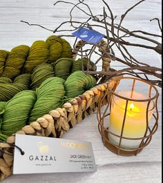 a basket filled with yarn next to a lit candle and business card on a table