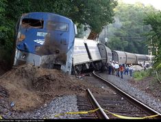 a train that is sitting on the tracks near some trees and people standing next to it