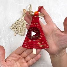 two hands holding an ornament in the shape of a bell and a christmas tree