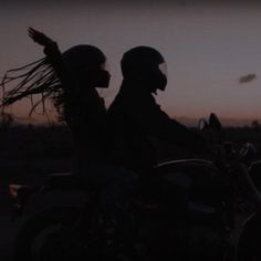 two people riding on the back of a motorcycle at sunset or dawn with long hair blowing in the wind