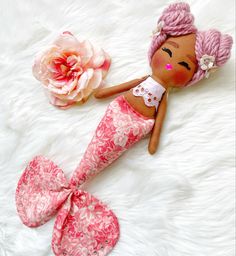 a doll laying on top of a white fur covered floor next to a pink flower