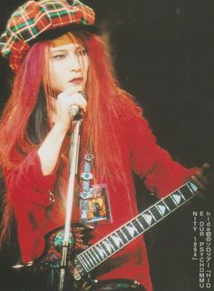 a woman with long red hair holding a guitar in her hand and singing into a microphone