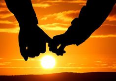 two people holding hands with the sun setting in the background