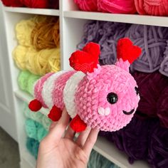 a hand is holding up a small stuffed animal in front of yarns on shelves