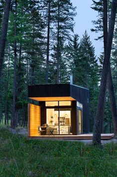 a small cabin in the woods with its lights on and windows lit up at night