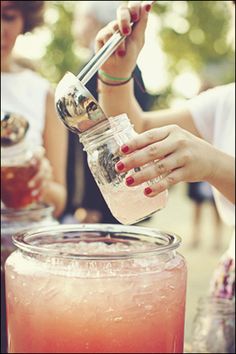 a woman is pouring something into a jar with a straw in it and another person behind her