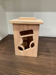 a wooden box with two holes in it on a wood floor next to a white wall