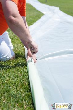 a person painting the side of a white sheet on grass with a pair of scissors