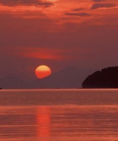 the sun is setting over an island in the middle of the ocean with mountains in the distance