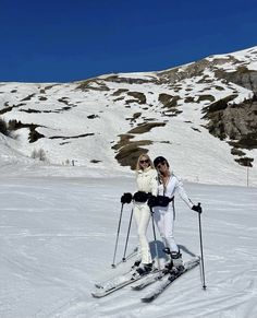 two people on skis pose for a photo in front of a snowy mountainside