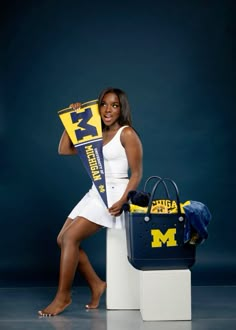 a woman is posing for a photo with her michigan scarf and purse in front of her