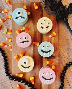 cupcakes decorated like faces and candy on a wooden board with halloween decorations around them