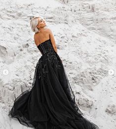 a woman in a black dress is standing on the sand and looking off into the distance