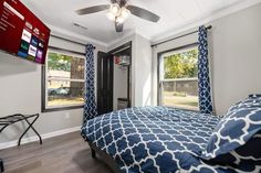 a bedroom with blue and white bedding, windows, and a flat screen tv