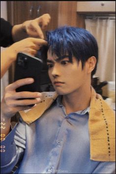 a man with blue hair is taking a selfie in front of a person holding a cell phone