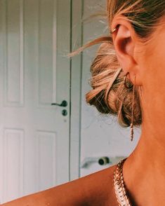 a woman wearing gold necklace and earrings looking at her cell phone in front of the mirror