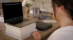 a woman sitting at a table with a stack of books and a laptop on top of it